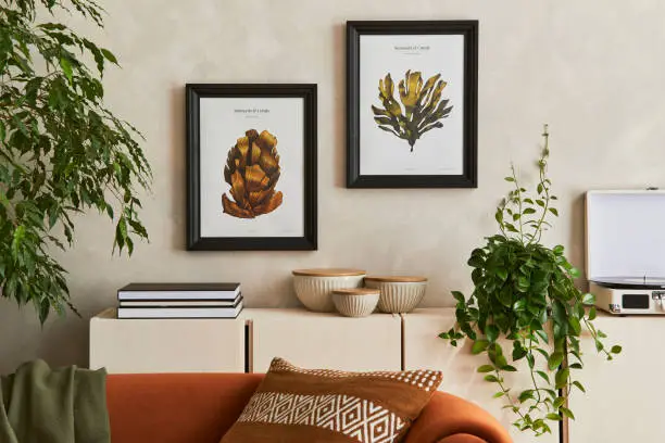 Creative composition of stylish living room interior with mock up poster frame, orange sofa, beige commode, coffee table and stylish personal accessories. Artistic space. Template.