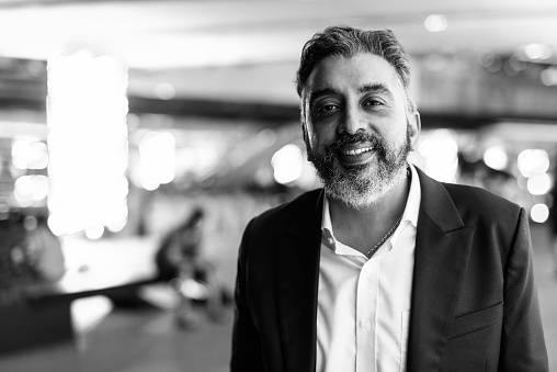 Portrait of handsome bearded Indian businessman outdoors at night shot in black and white