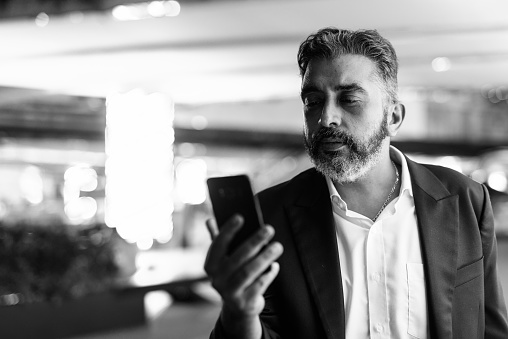 Portrait of handsome bearded Indian businessman outdoors at night shot in black and white