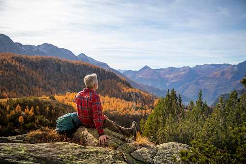 Hombre maduro descansando en el pico de la montaña, valle de la montaña de otoño photo