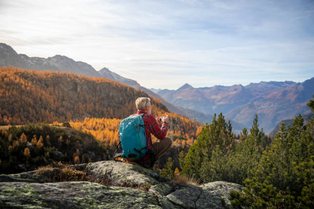 istock Hiker sitting on hill checking smartphone, autumn valley in background 1351072621