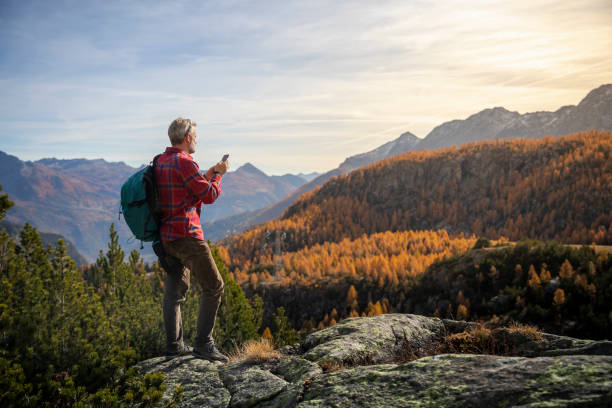 Hiker on mountain peak checking smartphone, autumn valley in background