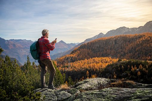Hiker on mountain peak checking smartphone, autumn valley in background
