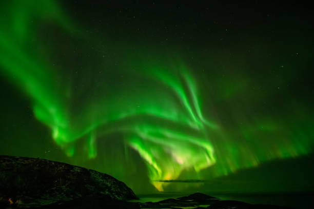 Aurora Borealis in the night sky over mountains silhouettes