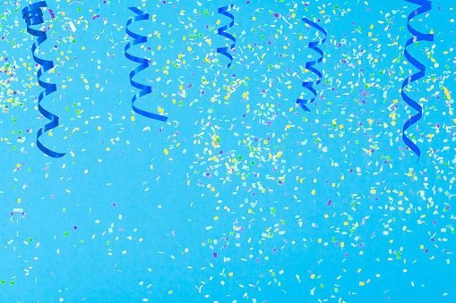 Birthday, party, celebration, New Year or Christmas celebration concept. Colored confetti and streamers falling against pastel colored blue background. High resolution 42Mp studio digital capture taken with Sony A7rII and Sony FE 90mm f2.8 macro G OSS lens