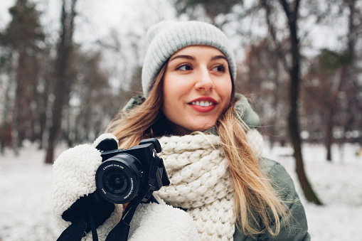 Woman photographer takes pictures of snowy winter park using camera wearing warm clothes. Outdoor hobbies, activities
