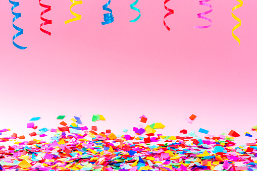 Birthday, party, celebration, New Year or Christmas celebration concept. Multicolored confetti and streamers shot against pastel colored pink background. Copy space available at the center of the frame. High resolution 42Mp studio digital capture taken with Sony A7rII and Sony FE 90mm f2.8 macro G OSS lens