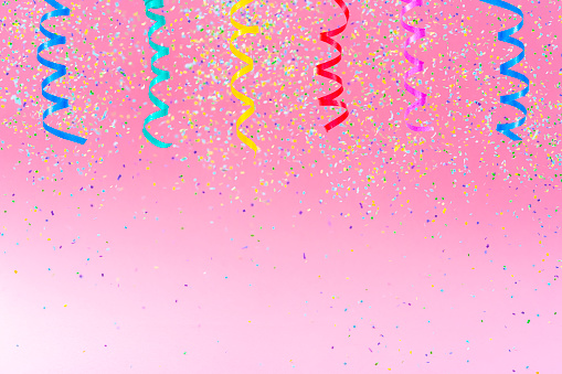 Birthday, party, celebration, New Year or Christmas celebration concept. Multi colored confetti and streamers falling against pastel colored pink background. High resolution 42Mp studio digital capture taken with Sony A7rII and Sony FE 90mm f2.8 macro G OSS lens