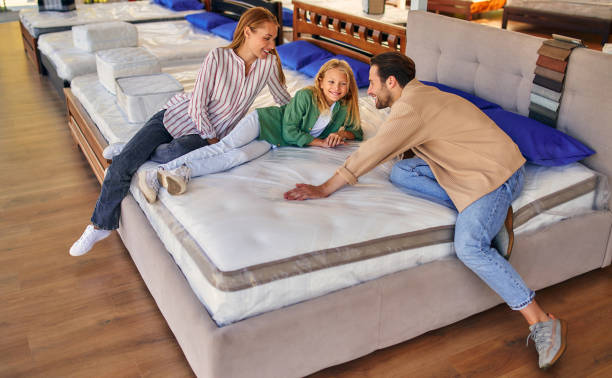 Beds, mattresses and pillows store A young family with their lovely daughter lay down on the bed, trying the mattress for softness in the store. Buying a bed and bedding. bed furniture stock pictures, royalty-free photos & images