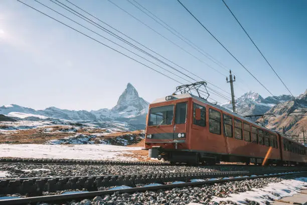 red train coming up mountain in the swiss alps with the matterhorn in the background