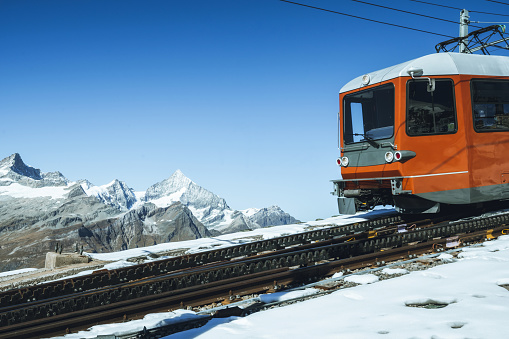 red train coming down mountain in the swiss alps with mountain range in the background