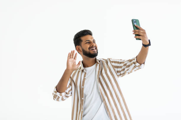 istock Indian young man with beard taking selfie using smartphone, isolated over white background 1351080601