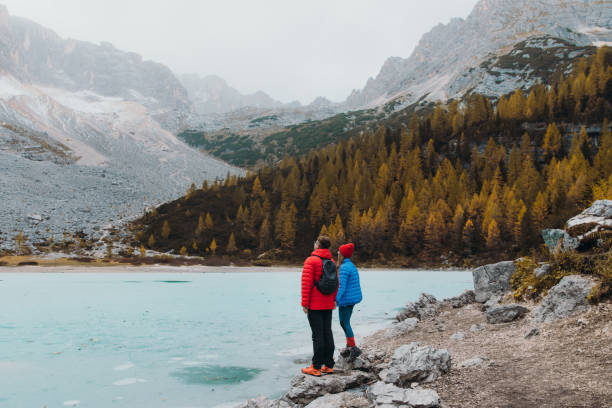 Photo of Female and male traveler staying on the rock enjoying the scenic view of the tuqouise frozen mountain lake in the Alps