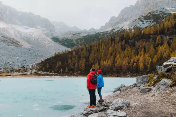 Young happy couple of backpackers got to the remote frozen crystal blue lake Sorapis in Dolomites Alps mountains during autumn time