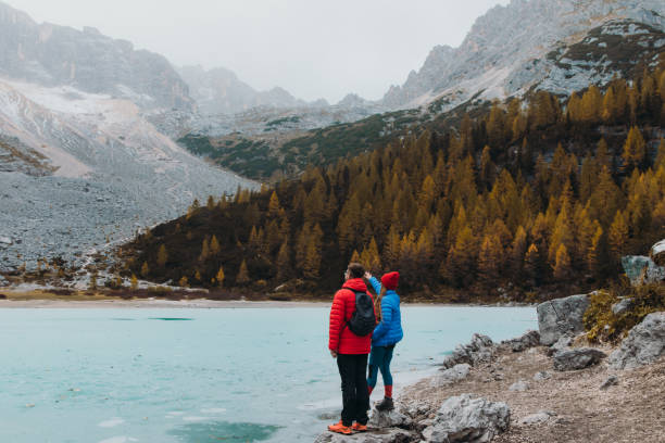 Photo of Female and male traveler staying on the rock enjoying the scenic view of the tuqouise frozen mountain lake in the Alps