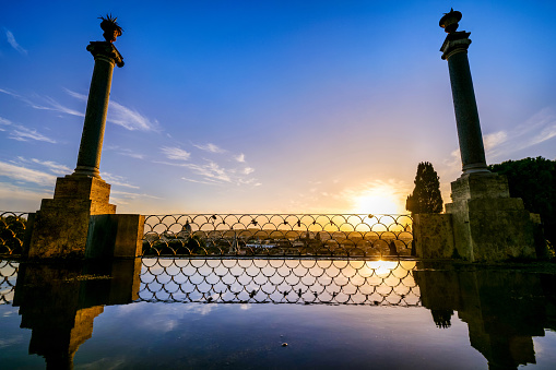 A random puddle of rainwater on the Pincio Gardens viewpoint reflects a suggestive sunset over the rooftops of Rome, in the historic and baroque heart of the Eternal City. The Pincio, one of the most visited and loved places in Rome, is the architectural culmination of Villa Borghese, the public park considered the green lung in the heart of the Italian capital. From this belvedere you can enjoy a breathtaking 180 degree view of the historic center of Rome, in the setting of some of the most beautiful gardens in the city. In 1980 the historic center of Rome was declared a World Heritage Site by Unesco. Super wide angle and high definition image.