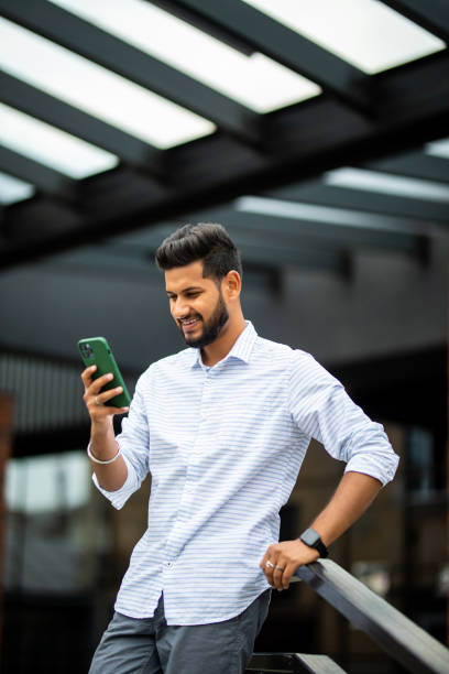 istock Indian handsome young businessman standing on the stairs while using his phone 1351083373