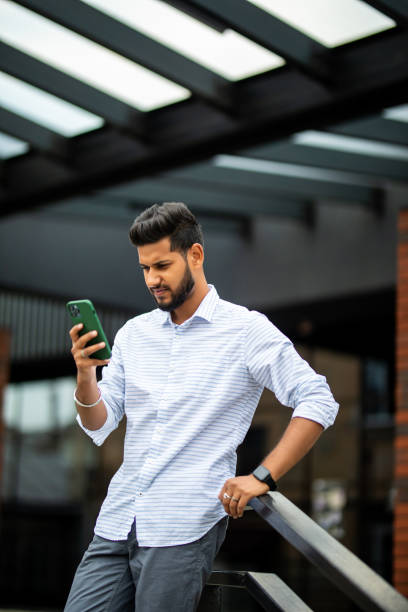 istock Indian handsome young businessman standing on the stairs while using his phone 1351084016