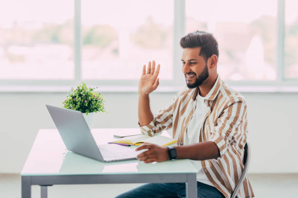 istock Young happy indian man talking on video conference call greeting waving hand using laptop at modern home office. Remote distant online communication technologies concept. 1351084603