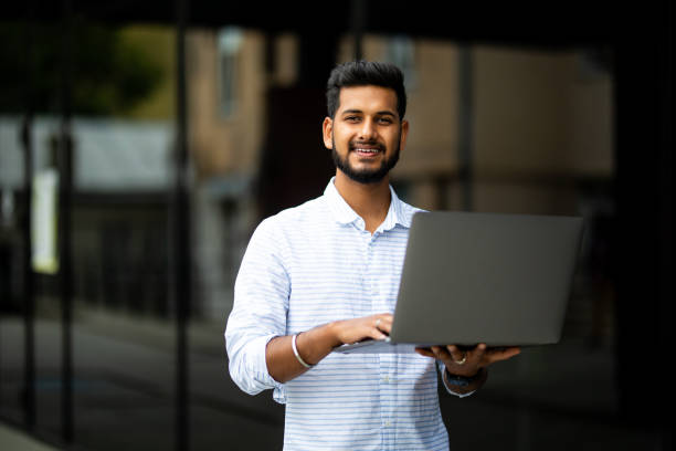 istock Young indian man working on the computer and drinking coffee on the street opposite the office 1351086006