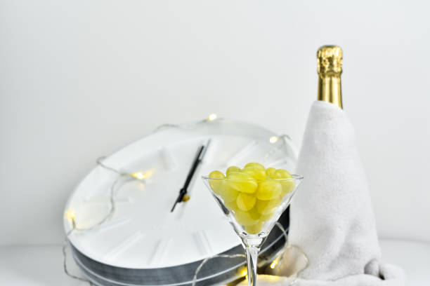 glas mit trauben auf dem hintergrund einer verschwommenen uhr und einer flasche champagner. spanische tradition, zwölf trauben zu essen, um neujahr zu feiern. - zwölf uhr stock-fotos und bilder
