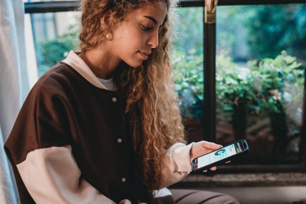 Young adult woman is checking her bank account Young adult woman is checking her bank account. She's holding a smart phone with a bank mobile app. Iphone stock pictures, royalty-free photos & images