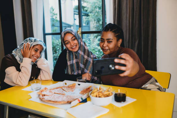 three friends are taking a selfie with a smart phone while they are eating pizza together - pizza eating african descent lunch imagens e fotografias de stock