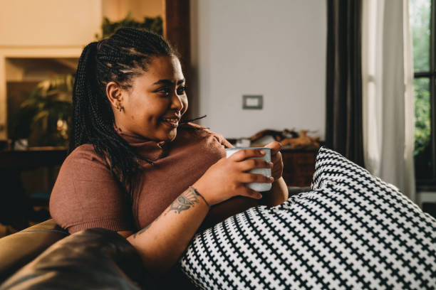 istock Mixed race woman is watching TV and drinking a coffee on the sofa 1351091171