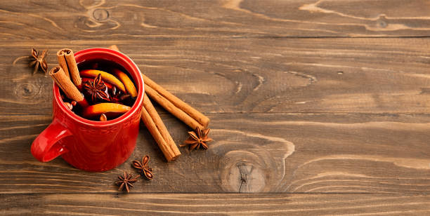 bebida alcohólica vino caliente en una taza roja con canela, naranja, clavo de olor se encuentra en una mesa de madera. lugar para su texto. - cider fotografías e imágenes de stock