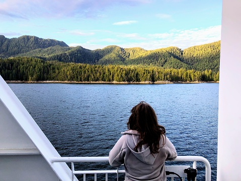 A woman standing on the deck of the inside passage ferry admiring the incredible views of the ocean and forest along the west coast of British Columbia, Canada