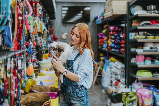 Young adult redhead woman enjoying in visit and shopping in petshop store together with her adorable Shih Tzu dog.