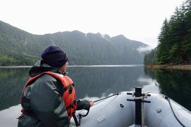 A woman at the front of a zodiac on a tour exploring the ocean, coastlines, forest and islands of Gwaii Haanas, Haida Gwaii, British Columbia, Canada. Beautiful scenery and calm ocean. stock photo