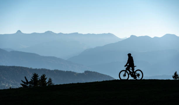 woman Silhouette on mountain bike in front of mountain summits Woman as silhouette riding her electric mountain bike in the Allgaeu alps near Oberstaufen with awesome view into the Bregenz Wald Mountains, Vorarlberg , Austria, people female mountain biker silhouette stock pictures, royalty-free photos & images