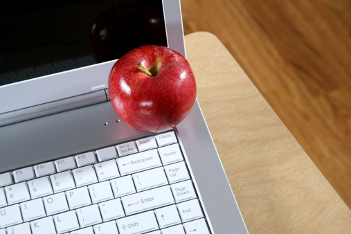 Red ripe delicious apple sitting on the edge of a computer in a school room. 