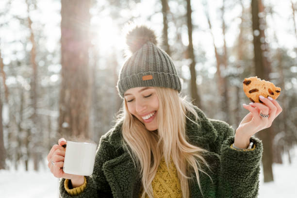 bella ragazza che gode dell'inverno all'aperto. belle donne che bevono cacao e si divertono nella foresta di neve - snow heat adult blond hair foto e immagini stock