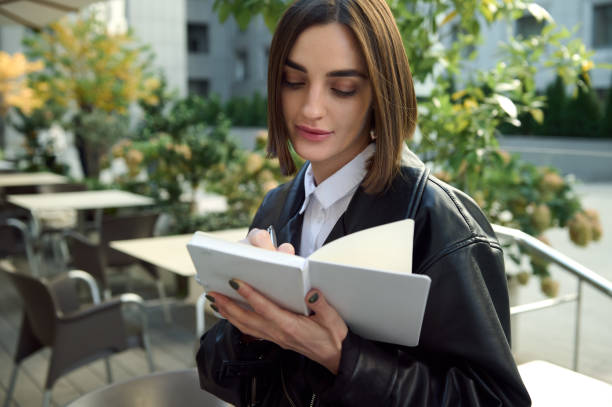 istock Confident portrait of focused young woman writing on white notepad while sitting outdoors on urban public background 1351103733