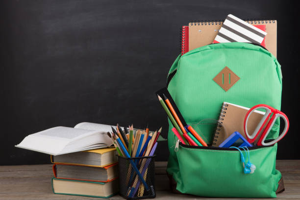 istock Education concept - school backpack with books and other supplies, blackboard background 1351103843