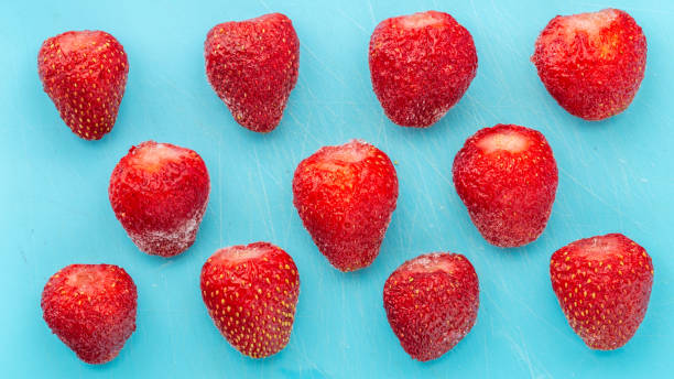 frozen strawberries are thawed on blue background. harvesting fruits and berries for the winter. frozen food close-up. - defreeze imagens e fotografias de stock