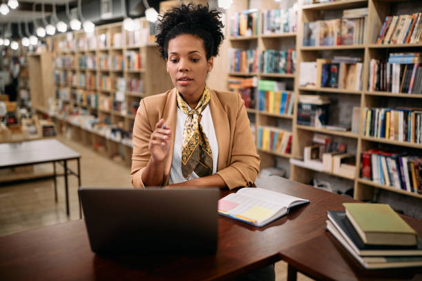 istock Black female teacher talking while holding online class over laptop from a library, 1351107540