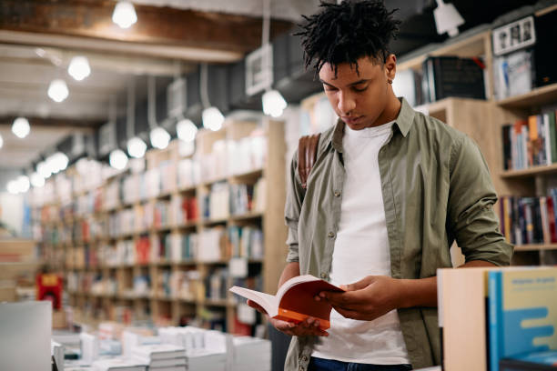 istock Young black student reading a book in a library, 1351107547