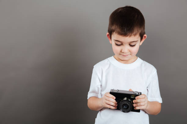 Cute little boy holding and using photo camera over grey background