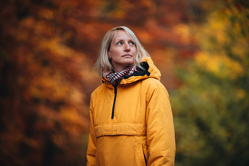 Close-up of a  young adult woman in a yellow jacket standing in the forest in the fall.