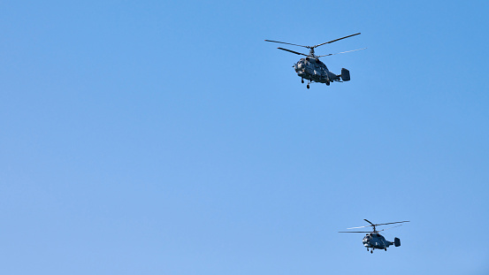 Two military helicopters flying in vibrant blue sky while performing demonstration flight, aerobatic team performs flight at air show, copy space