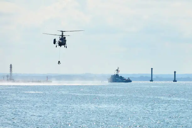 Battleship war ship corvette during naval exercises and helicopter maneuvering over water in Baltic Sea. Warships, helicopters and boats perform tasks in sea, military warships sailing, Russian Navy