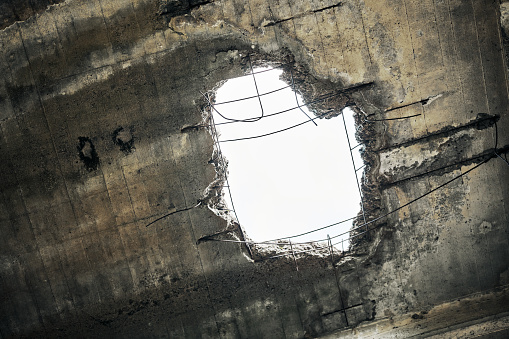 Vintage abandoned damaged house roof with hole in ceiling overlooking cloudy sky. Collapsed concrete wall with hole in abandoned industrial building, close up