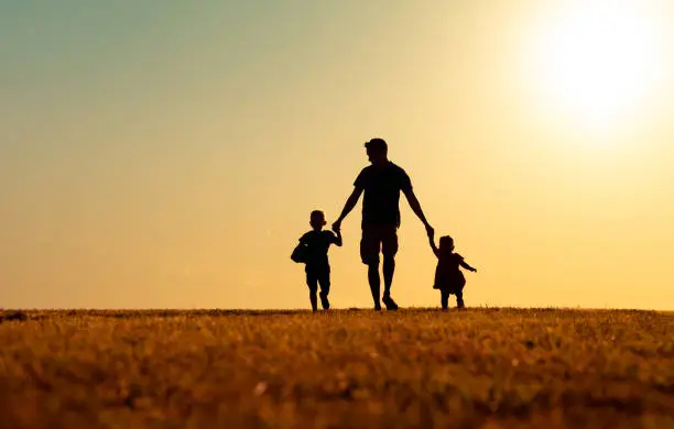 Photo of Father, son and daughter walking together at sunset.