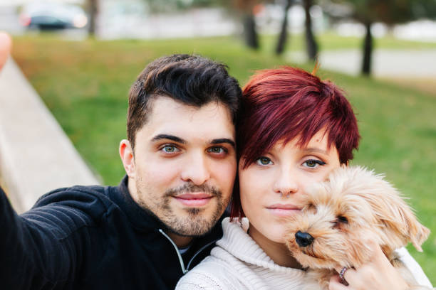 istock A young, handsome, light-eyed couple taking a selfie outdoors with their dog while walking in the city park. 1351146224
