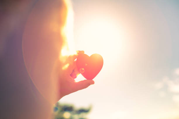 Little boy holding red heart against a beautiful sunset.