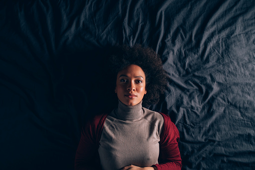 From above photo of young female resting in bed and looking at camera