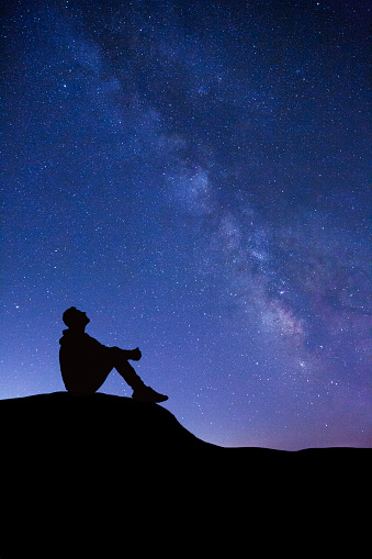 Silhouette of man sitting on the cliff looking at the Milky Way